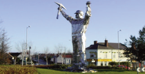 A statue of a coal miner with both arms held up one hand holding a pickaxe